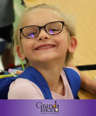  Smiling Engleman student with blonde hair and glasses holding an apple sauce cup in the cafeteria.