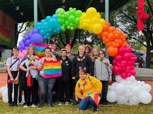 11 GISH LGTBQSA students and club sponsors standing with a rainbow balloon display