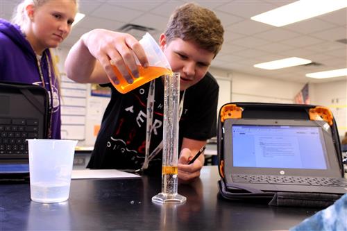 GISH students pouring orange liquid into a beaker in science class