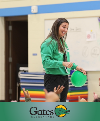  Mrs. Michel in her P.E. classroom holding a green balloon and smiling at kids raising their hands.