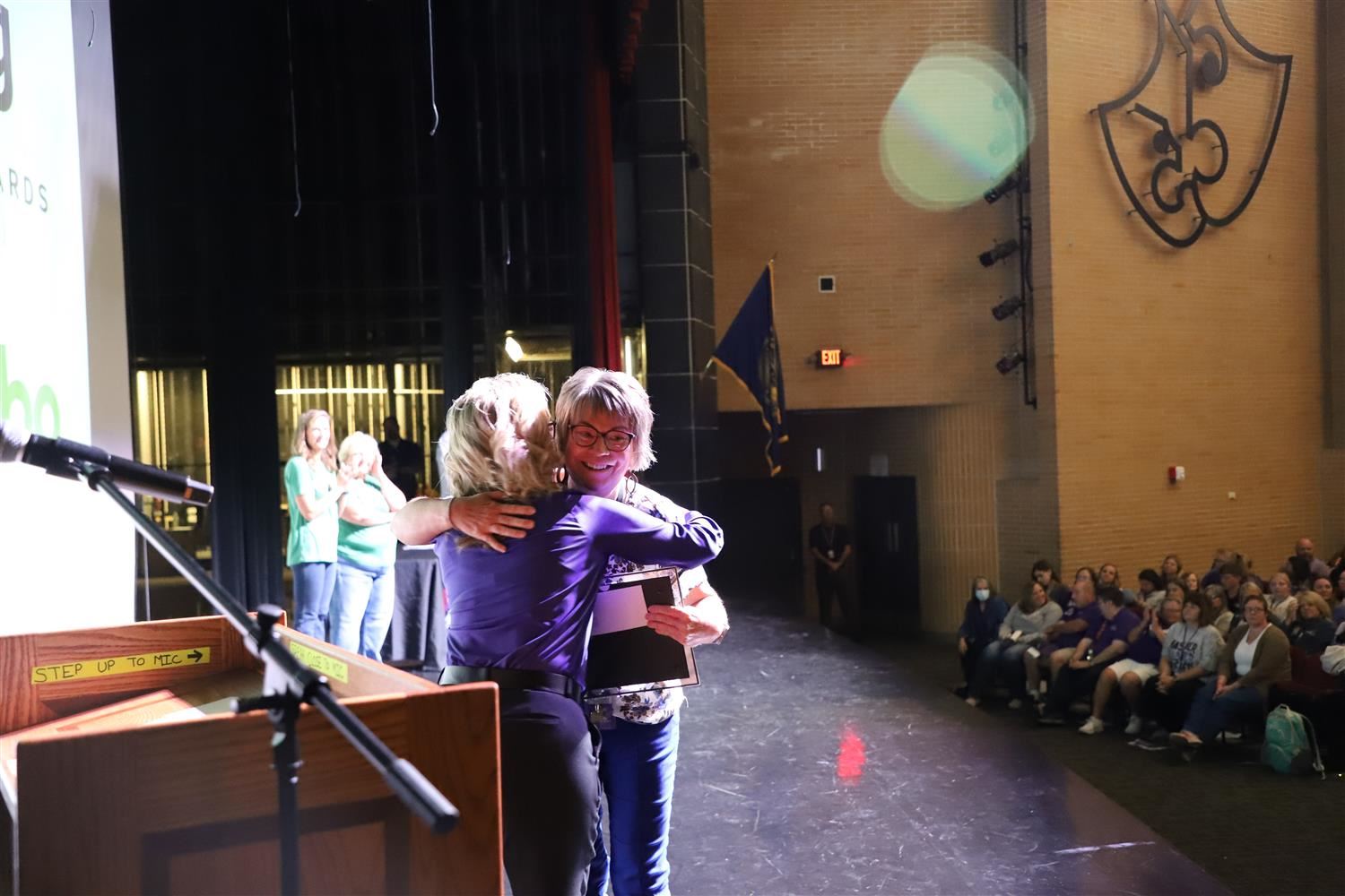 Michelle Enck accepting her Teacher of the Year Award on stage at GIPS Welcome Back and hugging GIPS Foundation Director.