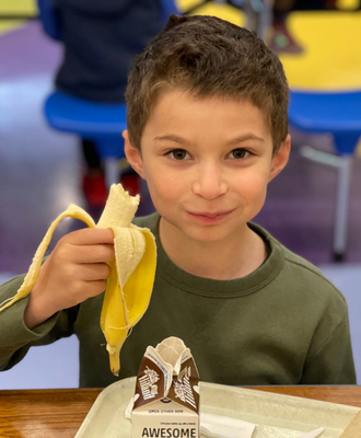  Smiling elementary student with a banana and milk carton in cafeteria