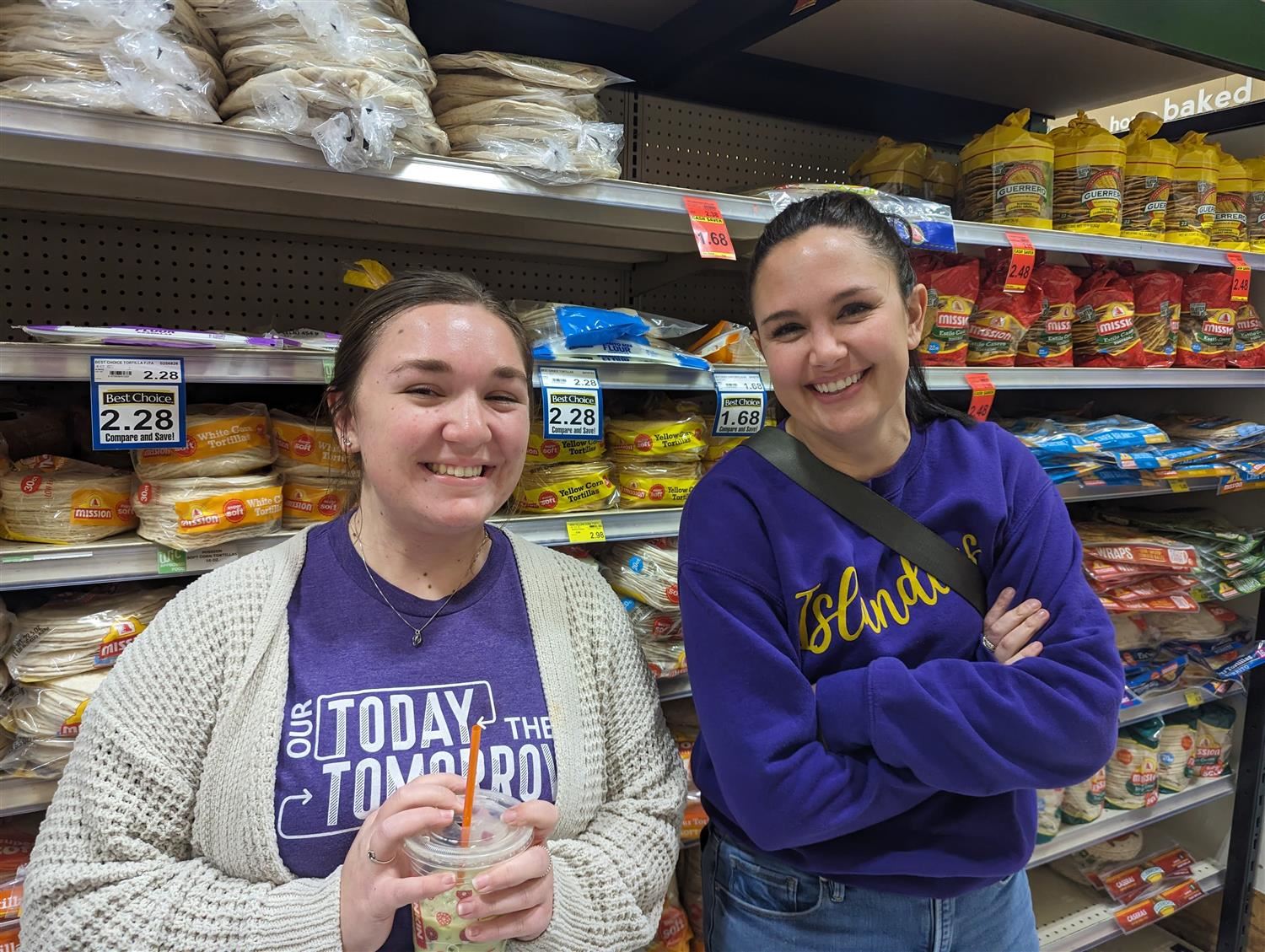 Two smiling Wasmer Elementary teachers helping families in the bread aisle at Super Saver.
