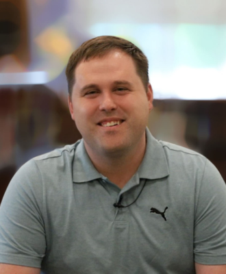  Mr. Jason Weseman sitting in a school library smiling.
